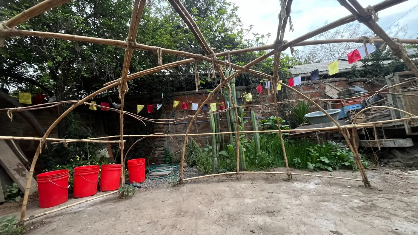 El domo del temazcal, hecho de varas amarradas, en el patio con cactus y banderitas de colores